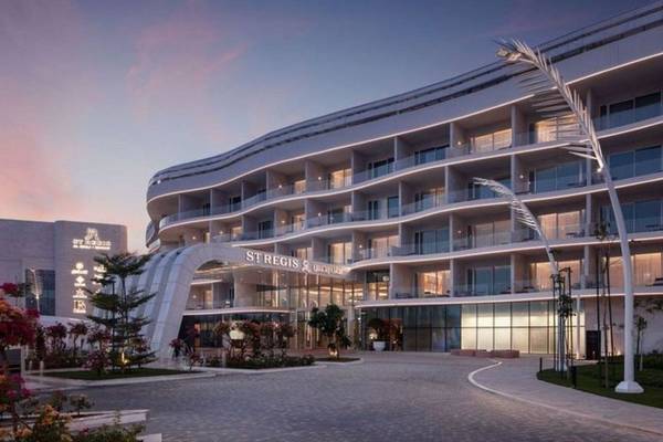 Außenansicht des St. Regis Al Mouj Muscat Resorts bei Nacht mit Beleuchtung und gepflanzten Gärten davor.