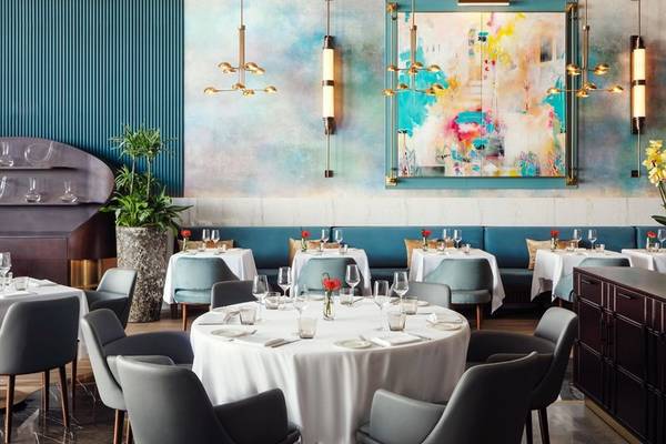 Innenraum des Restaurants im St. Regis Al Mouj Muscat Resort mit runden Tischen, modernen Möbeln und einer großen abstrakten Wandmalerei.