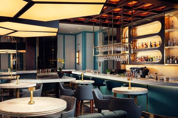 Innenansicht der Bar im St. Regis Al Mouj Muscat Resort mit Marmortischen, Stühlen und einer Theke mit vielen Flaschen.