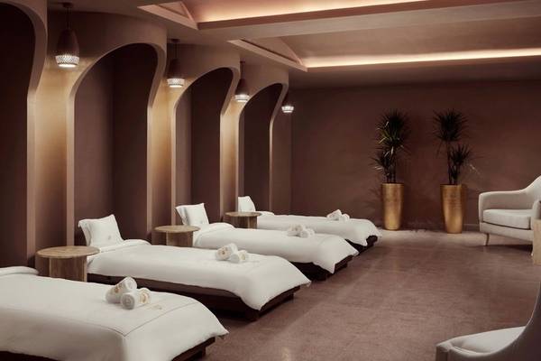 Spa-Behandlungsraum im St. Regis Al Mouj Muscat Resort mit mehreren weißen Liegen und goldenen Vasen.