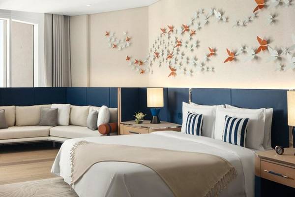 Schlafzimmer im St. Regis Al Mouj Muscat Resort mit großem Bett, Sofa, Nachttischen und blauen Kissen.