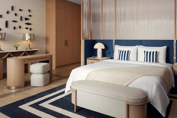 Inneneinrichtung eines Schlafzimmers im St. Regis Al Mouj Muscat Resort mit einem großen Bett, Nachttischen, Lampen und einem Schreibtisch.