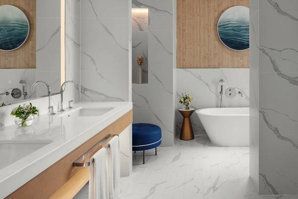 Badezimmer im St. Regis Al Mouj Muscat Resort mit Marmorwänden, zwei Waschbecken, Badewanne und Hocker.