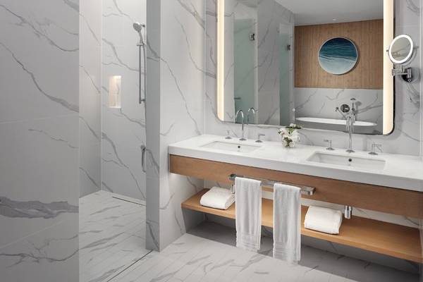 Das Badezimmer des St. Regis Al Mouj Muscat Resort mit weißen Marmorwänden und einem großen Spiegel.