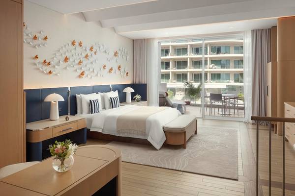 Innenansicht eines Zimmers im St. Regis Al Mouj Muscat Resort mit Bett, Nachttischen und Balkon.