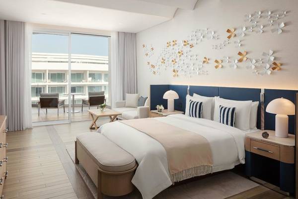 Schlafzimmer im St. Regis Al Mouj Muscat Resort mit großem Bett, Wanddekorationen und Blick auf Außenterrasse.
