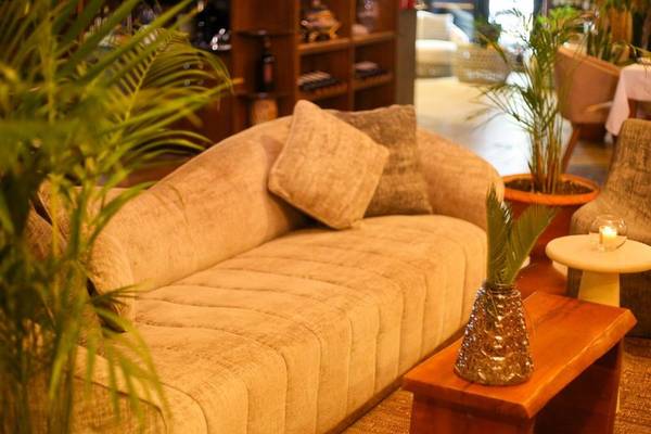 Hotellounge Bereich mit einem großen Sofa, Kissen, einem Tisch mit einer Glasvase und umgeben von Pflanzen.