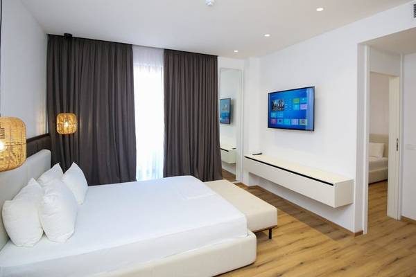 Hotelzimmer im Oricon Coast Luxury Resort mit einem großen Bett, weißen Kissen, einem Fernseher an der Wand und einem Fenster mit Vorhängen.