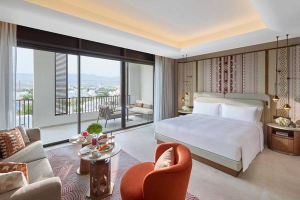 Suite Zimmer im Mandarin Oriental, Muscat mit Balkon, Bett, Couch, und Blick auf die Stadt.