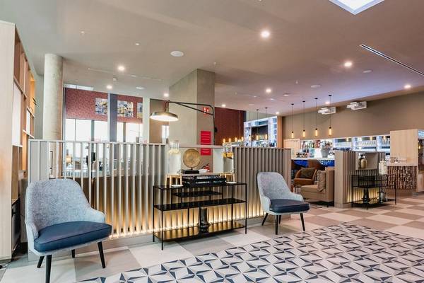 Lobbybereich des Leonardo Royal Hotel Barcelona Fira mit gemustertem Boden, Sesseln und Tischen.