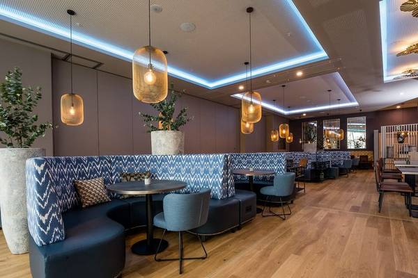Innenbereich des Leonardo Royal Hotel Barcelona Fira mit Sitzecken, Tischen und Holzboden.