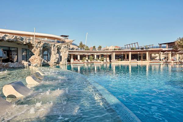 Außenansicht des Swimmingpools des Atlantica Caldera Palace Hotels mit Wasserfällen und Sonnenliegen.