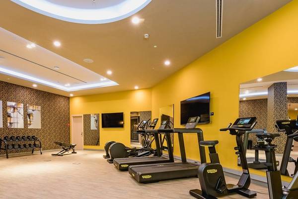Fitnessbereich im Leonardo Royal Hotel Barcelona Fira mit mehreren Trainingsgeräten und gelben Wänden.