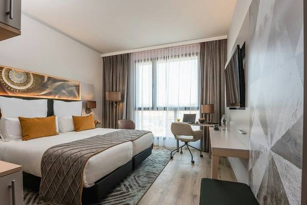 Schlafzimmer im Leonardo Royal Hotel Barcelona Fira mit zwei Betten, Schreibtisch und Fernseher.