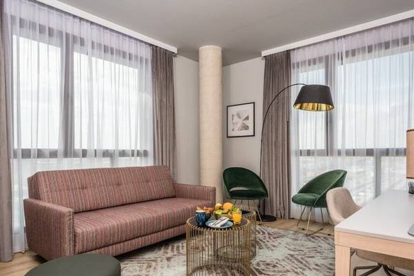 Wohnbereich des Leonardo Royal Hotel Barcelona Fira mit Sofa, Tisch, Lampen und Fenstern.
