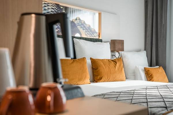 Bett im Zimmer des Leonardo Royal Hotel Barcelona Fira mit orangefarbenen Kissen und modernen Möbeln.