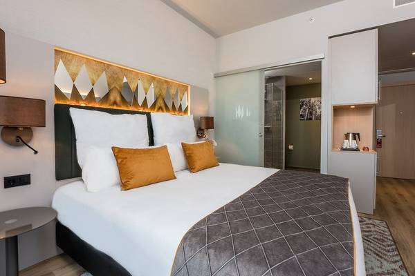 Innenansicht eines Schlafzimmers im Leonardo Royal Hotel Barcelona Fira mit einem Bett, Kissen, und einer modernen Einrichtung.