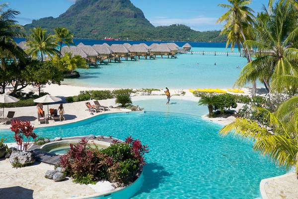Außenpoolbereich des Le Bora Bora by Pearl Resorts mit Überwasser-Bungalows und Berg im Hintergrund