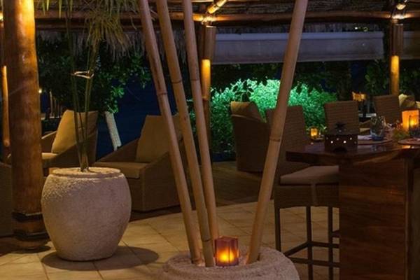 Terrasse im Le Bora Bora by Pearl Resorts mit Tischen, Stühlen und beleuchteten Bambusstangen.