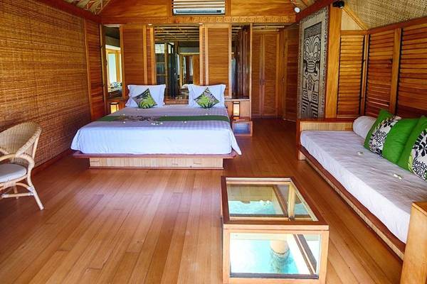 Innenansicht eines Zimmers im Le Bora Bora by Pearl Resorts mit einem großen Bett, einem Couchtisch und einem Couchsofa.