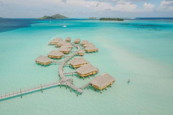 Luftaufnahme von Le Bora Bora by Pearl Resorts mit Wasserbungalows und Steg im kristallklaren Wasser