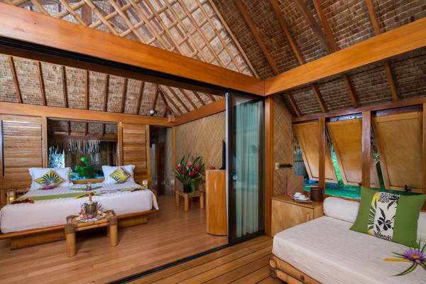 Innenansicht eines Zimmers im Le Bora Bora by Pearl Resorts mit einem Bett, Nachttischen und einer holzverkleideten Decke.