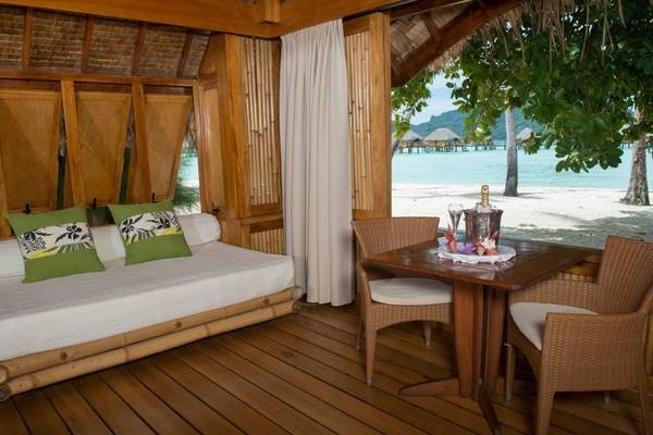 Innenbereich des Le Bora Bora by Pearl Resorts mit Bett, Tisch und Blick auf den Strand.