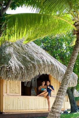 Paar, das vor einer Bambushütte von Le Bora Bora by Pearl Resorts sitzt