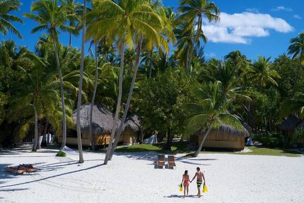 Le Bora Bora by Pearl Resorts Strand mit zwei Personen, die am Strand entlang gehen.