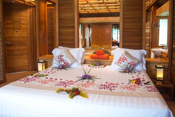 Schlafzimmer im Le Bora Bora by Pearl Resorts mit dekoriertem Bett und Holzmöbeln.