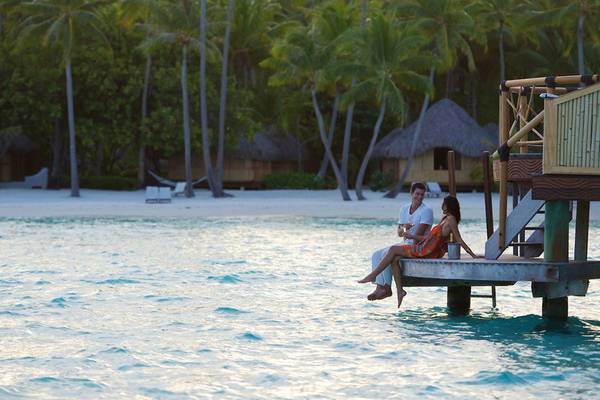 Ein Paar sitzt auf einer Holzplattform am Strand des Bora Bora by Pearl Resorts.