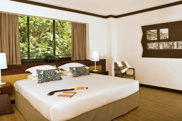 Schlafzimmer im Le Tahiti by Pearl Resorts Hotel mit großem Bett, Kissen, Lampe und Fenster mit Aussicht auf Bäume