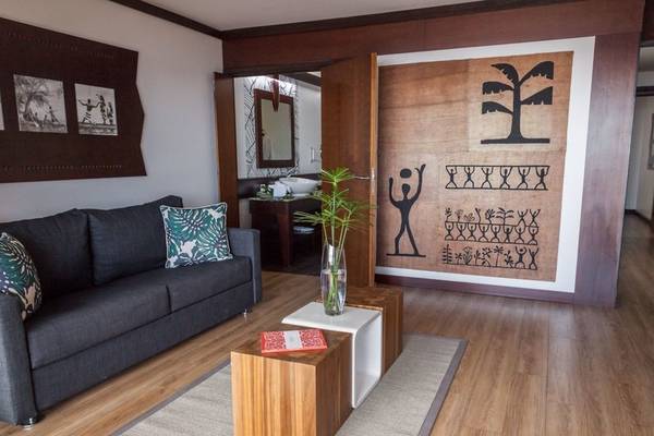 Wohnzimmer im Le Tahiti by Pearl Resorts mit grauem Sofa, Holztisch, Teppich und Wanddekoration.