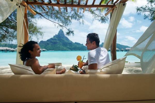 Ein Paar im InterContinental Bora Bora Resort genießt einen Drink unter einem Baldachin am Strand.