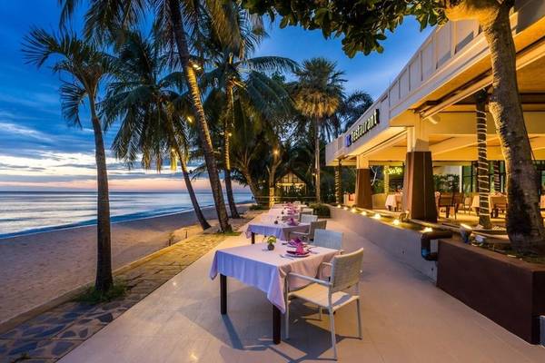 Außenbereich des KC Grande Resort Koh Chang mit Tischen und Stühlen, umgeben von Palmen, mit Blick auf den Strand und den Ozean bei Sonnenuntergang.