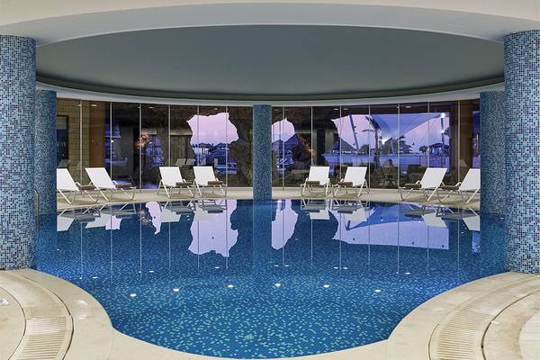 Innenpool des Atlantica Caldera Palace Hotels mit blauen Kacheln und weißen Sonnenliegen.