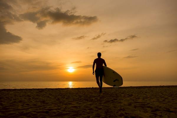 Mann mit Surfbrett am Strand bei Sonnenuntergang auf Koh Chang.