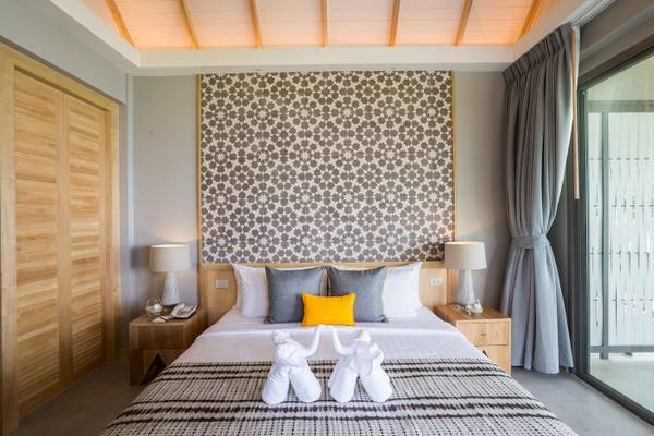 Schlafzimmer im KC Grande Resort Koh Chang mit gemusterter Wand, zwei Nachttischen, Lampen, Telefon und zwei weißen Elefanten-Handtüchern.