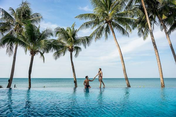 Ein Paar im Infinity-Pool vor Palmen und Meer am KC Grande Resort Koh Chang