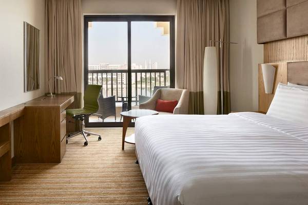 Hotelzimmer im Traders Hotel Qaryat Al Beri mit Fernseher, Schreibtisch, Stühlen und Balkon.