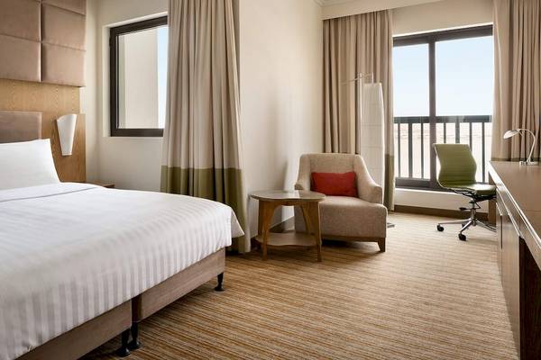 Ein elegantes Hotelzimmer im Traders Hotel Qaryat Al Beri mit einem Bett, einem Schreibtisch und einem Fenster mit Blick auf die Stadt.