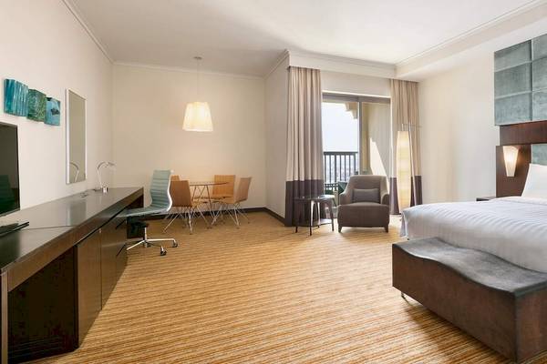 Hotelzimmer im Traders Hotel Qaryat Al Beri mit Schreibtisch, Stühlen, Tisch, Fernseher und Bett.