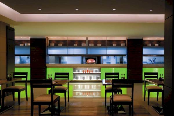 Innenansicht des Restaurants im Traders Hotel Qaryat Al Beri mit grünen Wänden und dunklen Möbeln.