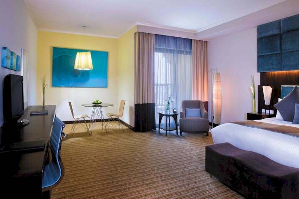 Hotelzimmer im Traders Hotel Qaryat Al Beri mit Bett, Schreibtisch und Wohnzimmerbereich.