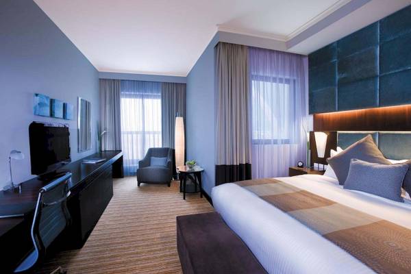 Interieur eines Schlafzimmers im Traders Hotel Qaryat Al Beri mit Bett, Fernseher, Stuhl und Schreibtisch.
