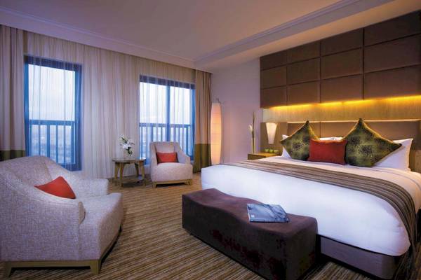 Suite-Zimmer im Traders Hotel Qaryat Al Beri mit großem Bett, Sesseln und Fenstern.