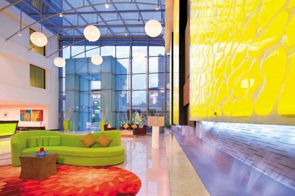 Hotellobby des Traders Hotel Qaryat Al Beri mit grüner Couch, rotem Teppich und gelber Wand