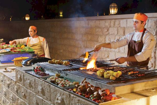 Grill im Traders Hotel Qaryat Al Beri mit Köchen, die Fleisch und Gemüse zubereiten.