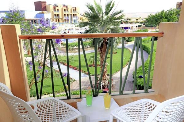 Ein Balkon mit Blick auf ein Hotel und einen Pool, zwei weiße Stühle und ein Tisch mit Getränken.