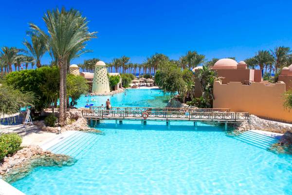 Ein großer Poolbereich des Grand Makadi Hotels mit einer Brücke und mehreren Palmen im Hintergrund.